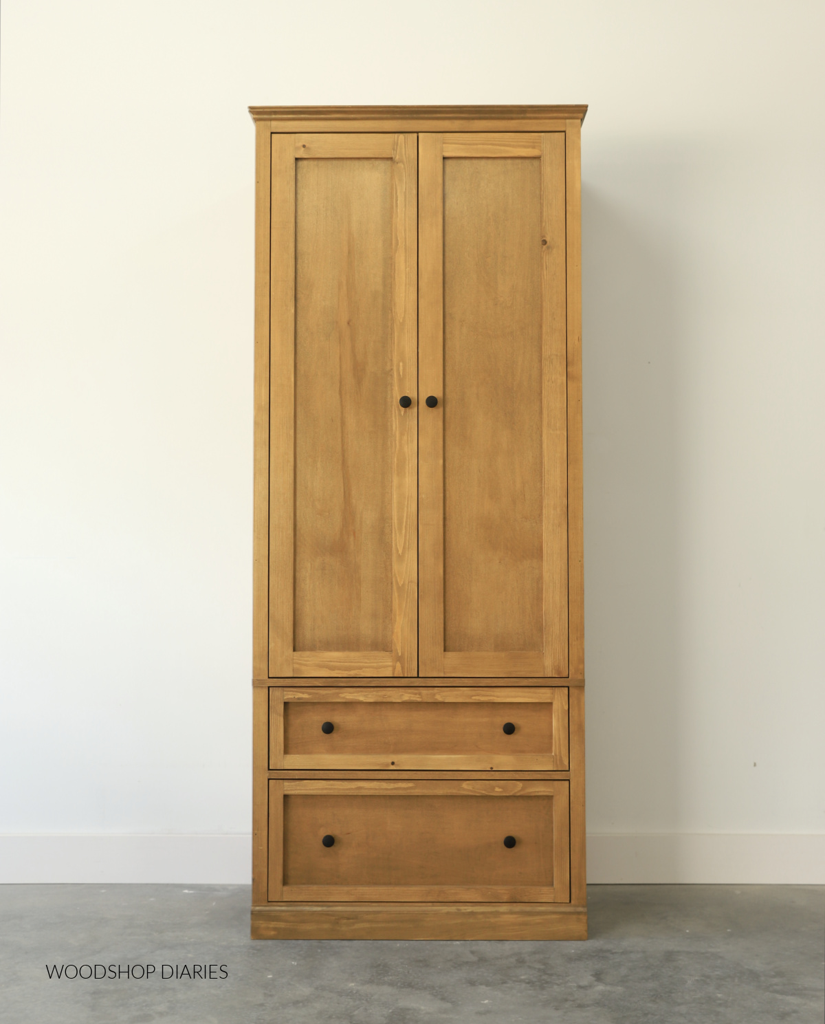 Completed DIY armoire cabinet with double doors at top and two drawers at bottom finished in custom stain against white wall