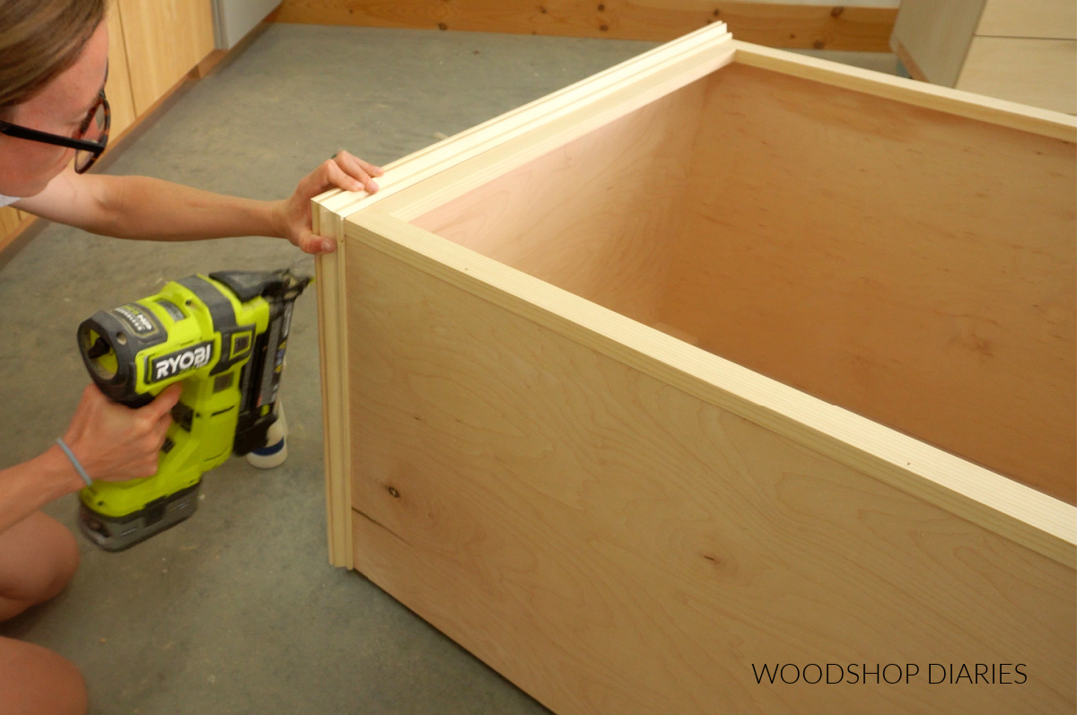 Close up of Shara Woodshop Diaries brad nailing base cap molding around sides of cabinet at top