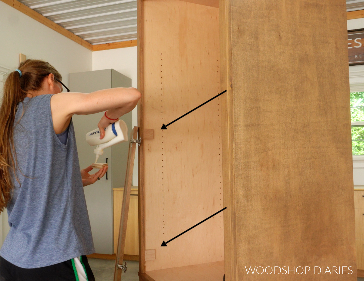 Shara Woodshop Diaries applying glue to hinge spacer block. Arrows pointing to already installed blocks in cabinet