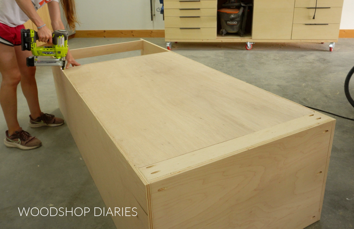 Shara Woodshop Diaries stapling back panel of cabinet onto cabinet box on workshop floor