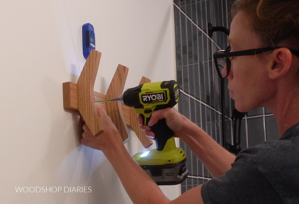 Shara Woodshop Diaries hanging scrap wood towel rack onto bathroom wall with screws