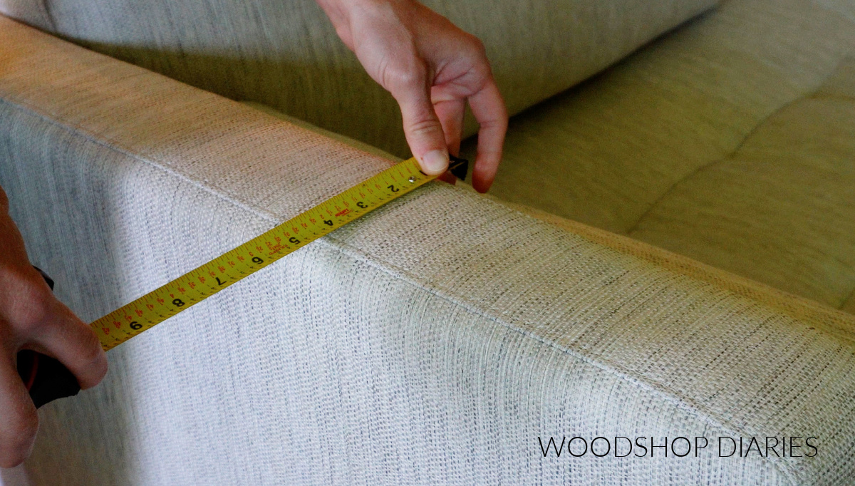 Close up of Shara Woodshop Diaries measuring sofa arm width using tape measure
