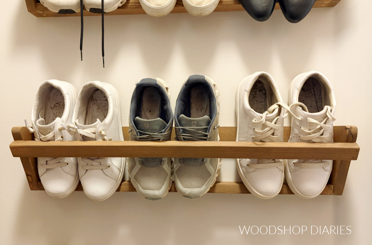 Wooden shoe rack mounted onto closet wall with three pair of sneakers resting inside