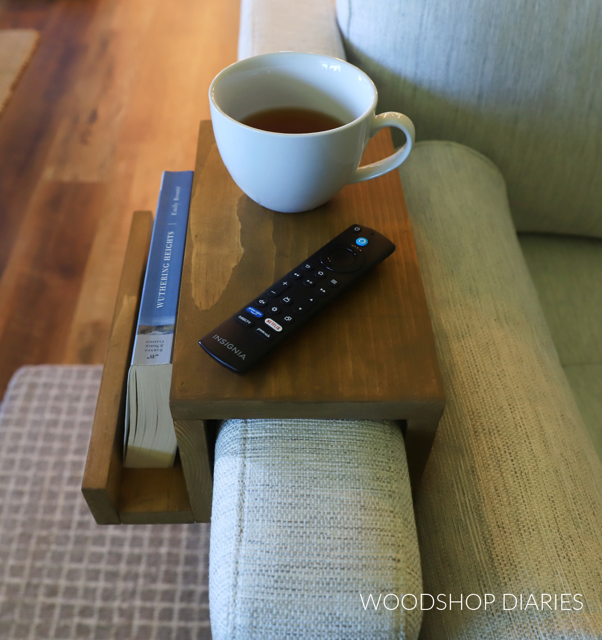Wooden sofa armrest caddy on white sofa with book, remote, and tea