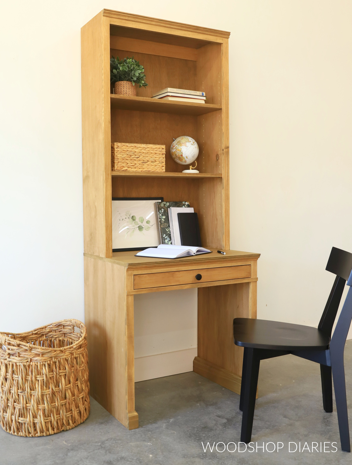 DIY desk with bookcase hutch against white wall with black chair and basket next to it